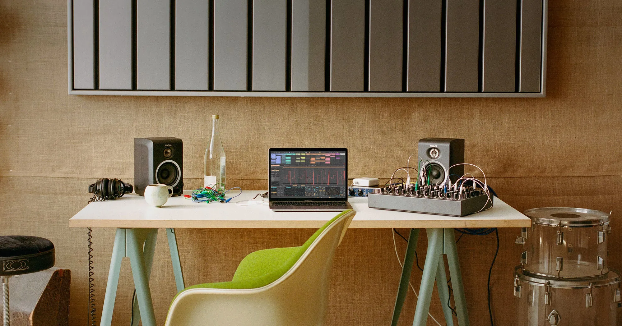 A laptop on a studio desk between monitor speakers, a modular synth and a drum kit.